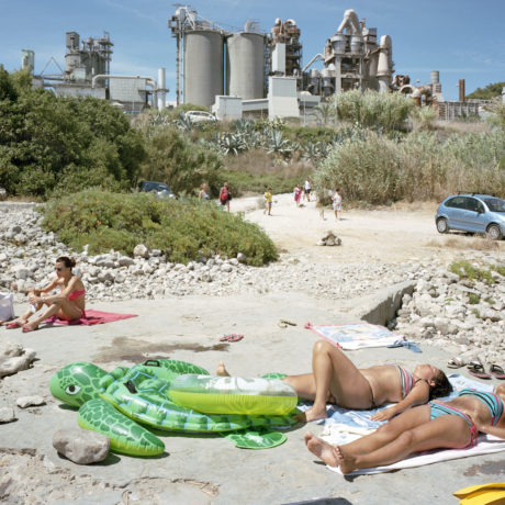 Throughout the series, which has just been published as a book by Mack, sun-seekers set up camp in car parks; swimming pools appear as mini oases in a desert of grey concrete; and cranes and cooling towers loom awkwardly over beaches. The contrast between these built up, man-made environments and the sunbathers, who appear minute in scale, is amusingly surreal, but highlights our subservience towards industry, housing developments and superstores.