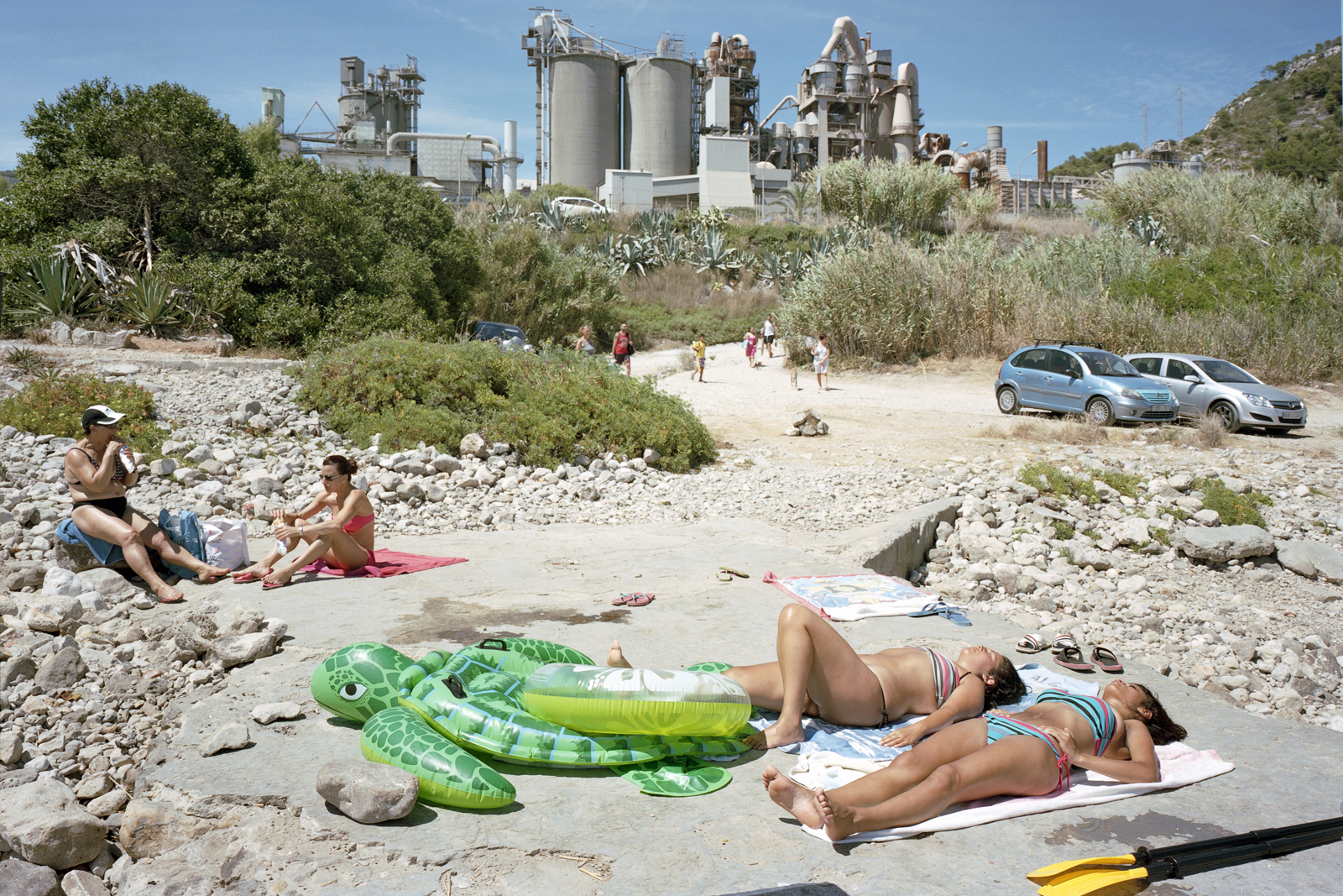 Throughout the series, which has just been published as a book by Mack, sun-seekers set up camp in car parks; swimming pools appear as mini oases in a desert of grey concrete; and cranes and cooling towers loom awkwardly over beaches. The contrast between these built up, man-made environments and the sunbathers, who appear minute in scale, is amusingly surreal, but highlights our subservience towards industry, housing developments and superstores.